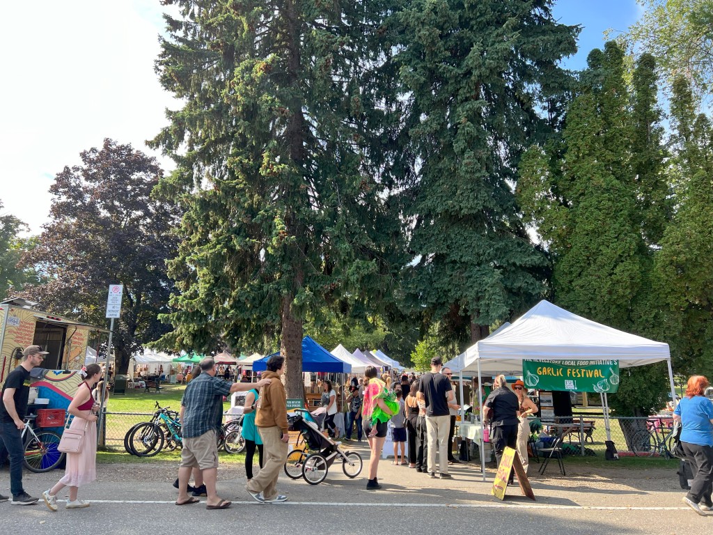 Vendors line a path with walkers and bike riders going past them at Garlic Fest 2024.